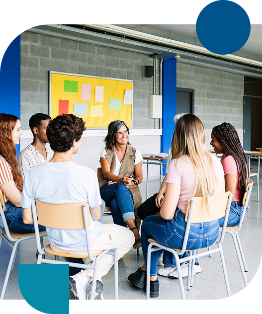 Teacher leading group discussion with teenagers seated in a circle in classroom.
