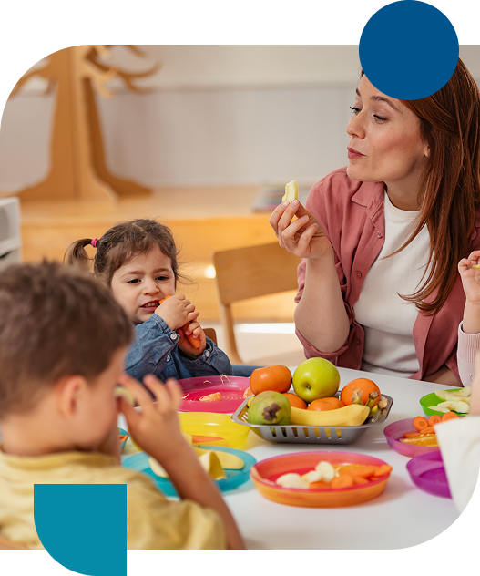 Teacher smiling while helping a girl in a wheelchair at a classroom table.
